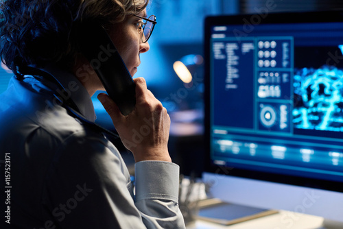 Focus on mature woman in uniform holding phone receiver by ear and looking at computer screen while reporting about situation
