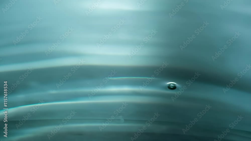 Drops of Crystal Clear Water. A drop of liquid slowly falls on the water surface. A beautiful splash and circles on the water