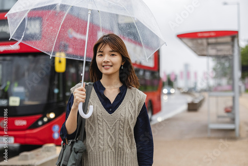 Photography Young woman holding transparent umbrella at london bus stop
