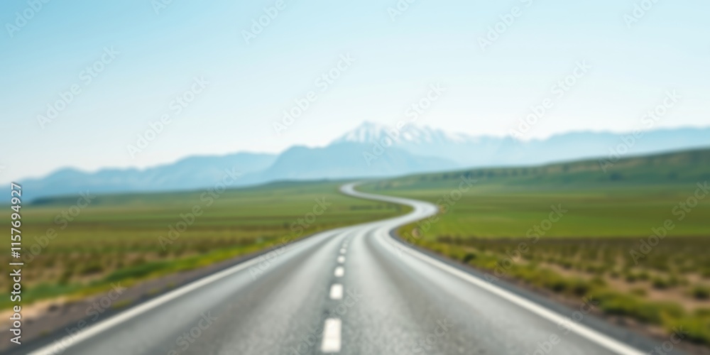 Fototapeta premium Asphalt Road Winding Through a Verdant Meadow Towards Majestic Mountains Under a Clear Sky