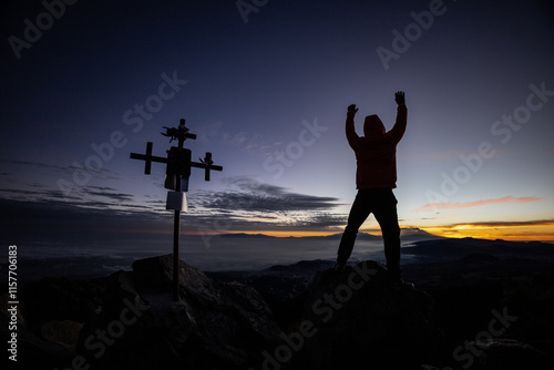 Man celebrating sunrise atop mountain with silhouetted cross photo