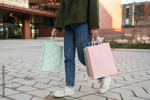Woman in casual outfit carrying pastel shopping bags outdoors