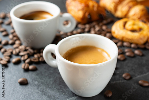 two cups of coffee on slate, coffee beans scattered on slate, cinnamon roll, croissant and pain au chocolate