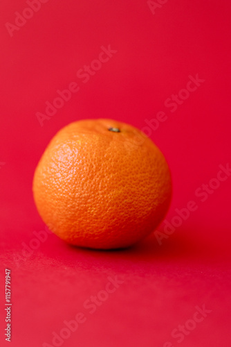 unpeeled mandarin on red background, one tangerine side view from close up on bright red background