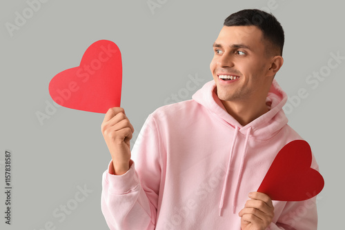 Happy young man with red paper hearts on grey background