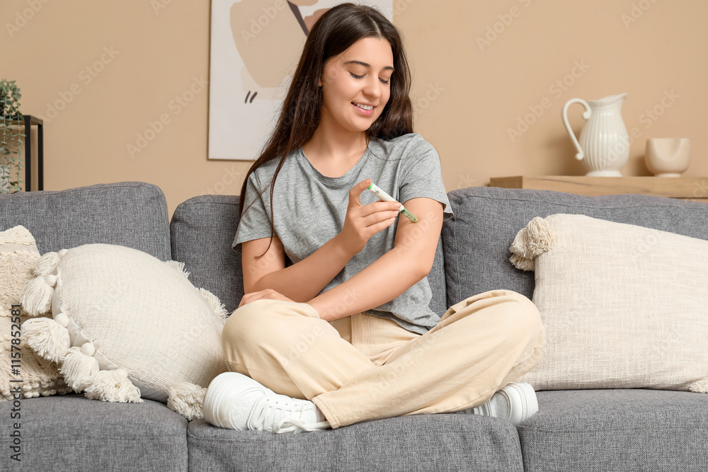 Obraz premium Diabetic young woman using lancet pen on sofa at home