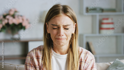 Fotografie Young woman crying on the sofa at home, eyes closed and tears streaming down her