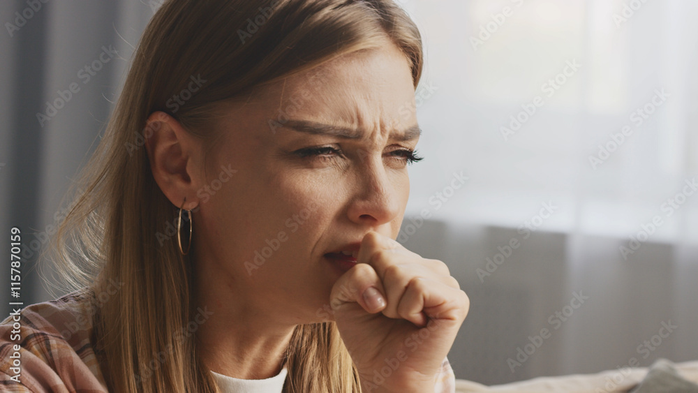 Young woman suffering from cough, covering her mouth with hand while sitting on sofa at home, experiencing symptoms of illness, feeling unwell and needing medical attention Young woman suffering from cough, covering her mouth with hand while sitting on sofa at home, experiencing symptoms of illness, feeling unwell and needing medical attention