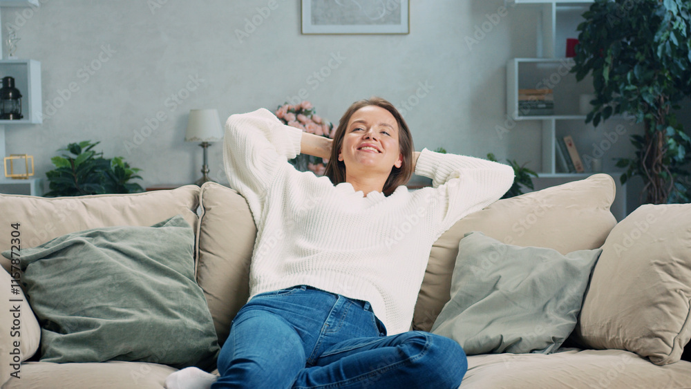 Smiling woman is lying on comfortable sofa with her hands behind her head, enjoying her leisure time in cozy living room, feeling relaxed and happy Smiling woman is lying on comfortable sofa with her hands behind her head, enjoying her leisure time in cozy living room, feeling relaxed and happy