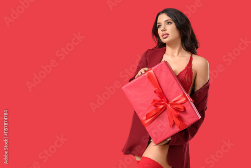 Sexy young woman in underwear and blazer with gift box on red background. Valentine's Day celebration