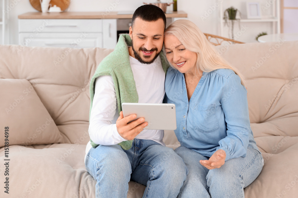 Young man with tablet computer hugging his mother on sofa in kitchen Young man with tablet computer hugging his mother on sofa in kitchen