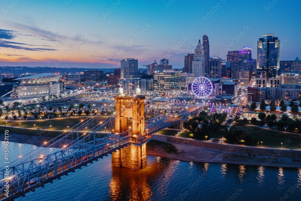 Fototapeta premium Evening cityscape view of the Cincinnati skyline, featuring the iconic Roebling Suspension Bridge at twilight. Downtown, Cincinnati, Ohio, United States