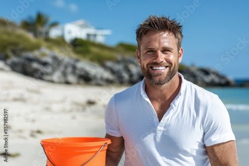 A man in a white shirt, smiling with an orange bucket, enjoys a beautiful sunny day at a beach with rocky background, capturing a quintessential summer moment.