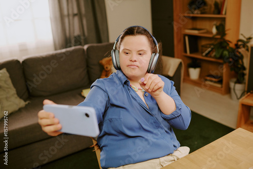 High angle view of creative girl with Down syndrome demonstrating flower-shaped bead while taking selfie on smartphone photo