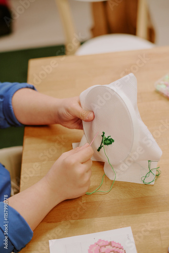 Vertical high angle medium closeup of unrecognizable female hands holding hoop with fixed fabric embroidering flower