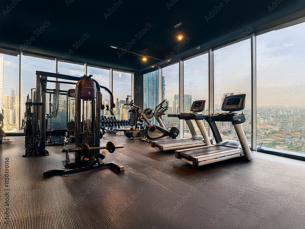 Modern gym with floor-to-ceiling windows offering a stunning city view. State-of-the-art equipment is available for a productive workout. Modern gym with floor-to-ceiling windows offering a stunning city view. State-of-the-art equipment is available for a productive workout.