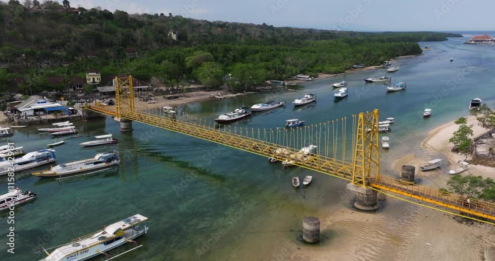 Aerial medium tracking right slowly above Nusa Ceningan bridge connecting vibrant coastal establishing view with boats