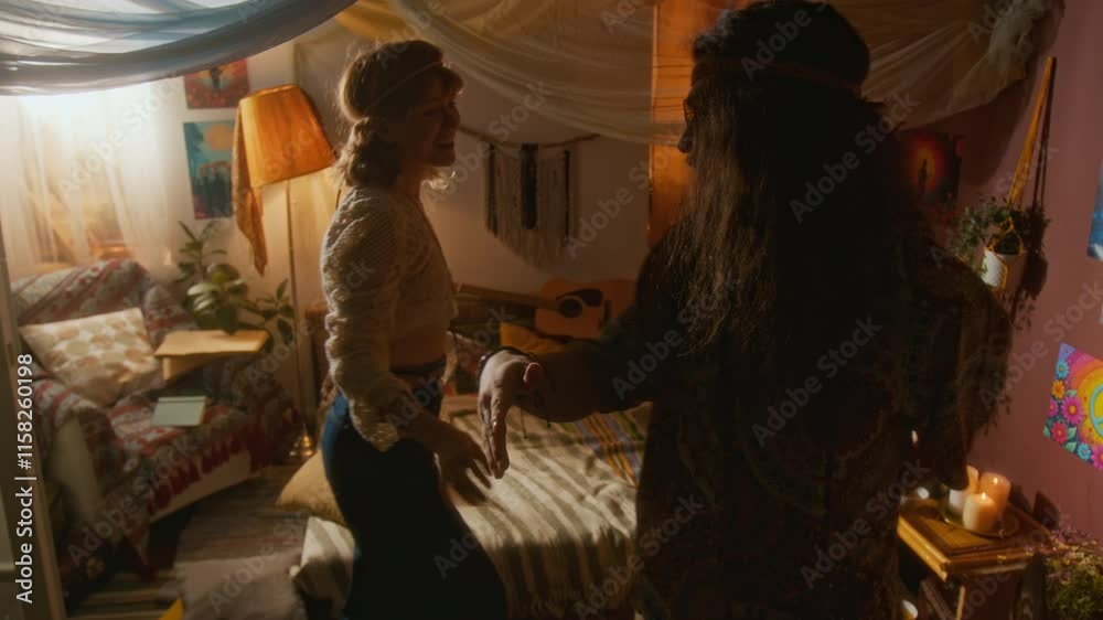 Medium full shot of cheerful, happy Caucasian hippie couple with long hair, in stylish outfits dancing together to vinyl record in bedroom, smiling, laughing, while spending weekend at home