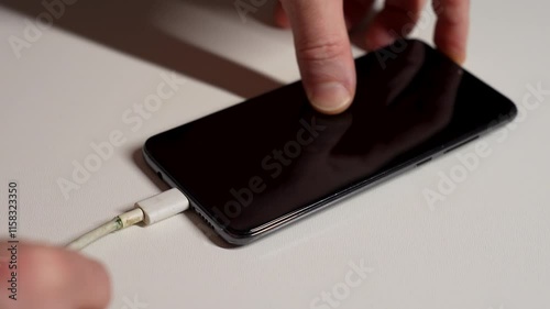 Charging phone with broken charging cable, close-up. Hand holding frayed charging cable type C