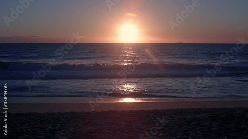 Waves mildly crashing onto the beach in a sunset facing the Great Australian Bight, a ship slowly cruises on in the horizon