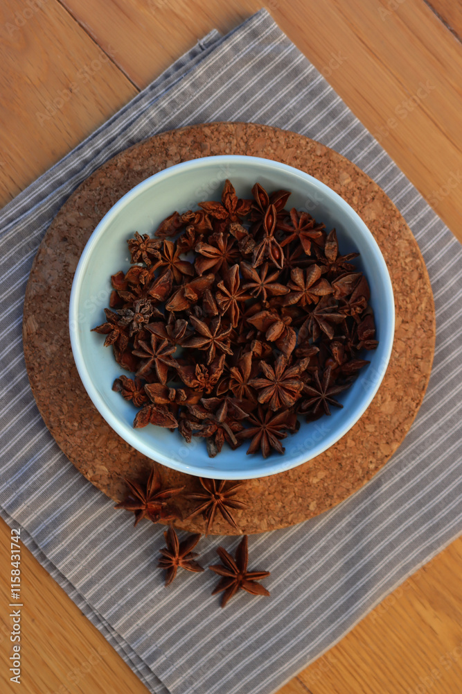 Top view of dry Anise stars spices in a blue ceramic bowl on wooden table. Illicium verum Top view of dry Anise stars spices in a blue ceramic bowl on wooden table. Illicium verum