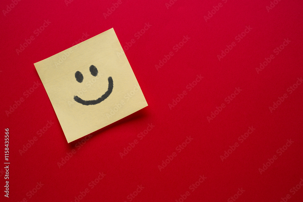 Smiley face emoji drawing on sticky note paper on red background Smiley face emoji drawing on sticky note paper on red background