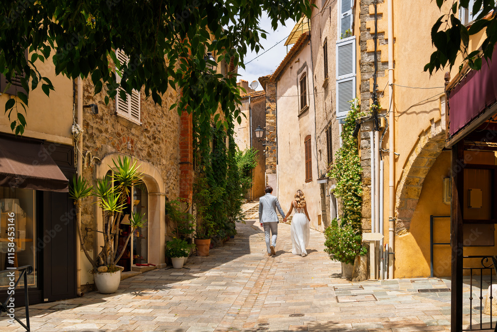 Obraz premium A nicely dressed young couple walk through the narrow streets of the medieval hill town of Grimaud, France, in the hills above St Tropez on the French Riviera.