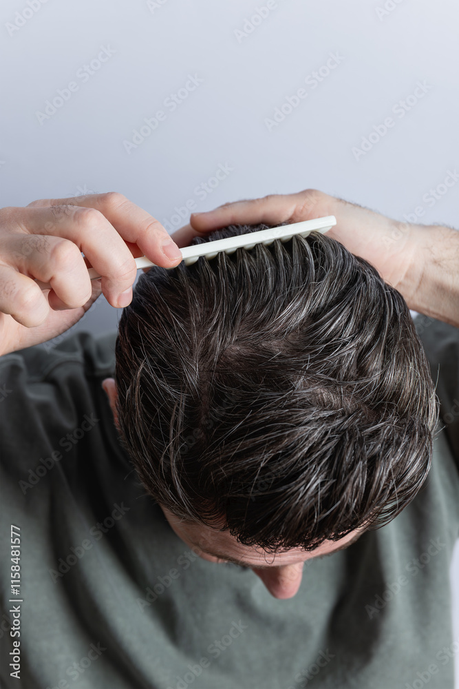 Naklejka premium Close up of hair of an unrecognizable man combing his hair with his hands and a comb. Copy Space. Concept of hairstyle and hair care