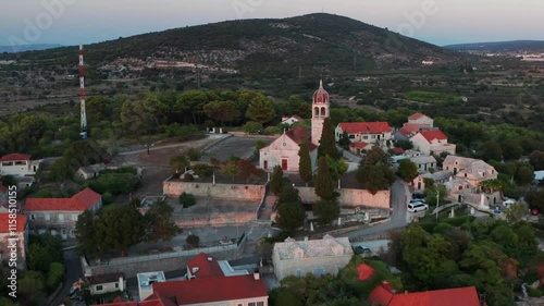 Donji Humac on Brac Island, Croatia. Backward drone flight reveals small town and green hills on the horizon photo