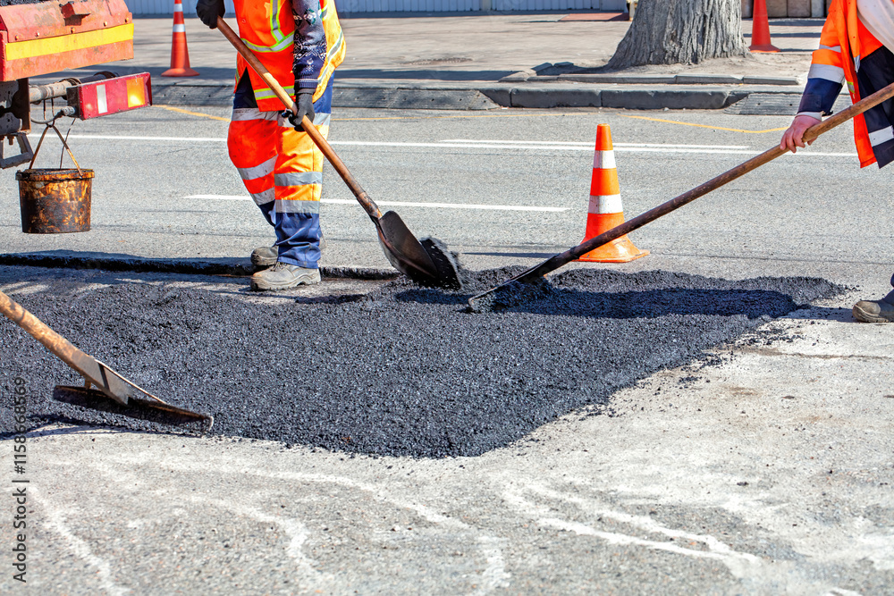 Road workers repair pavement on a sunny day with bright orange cones marking the site