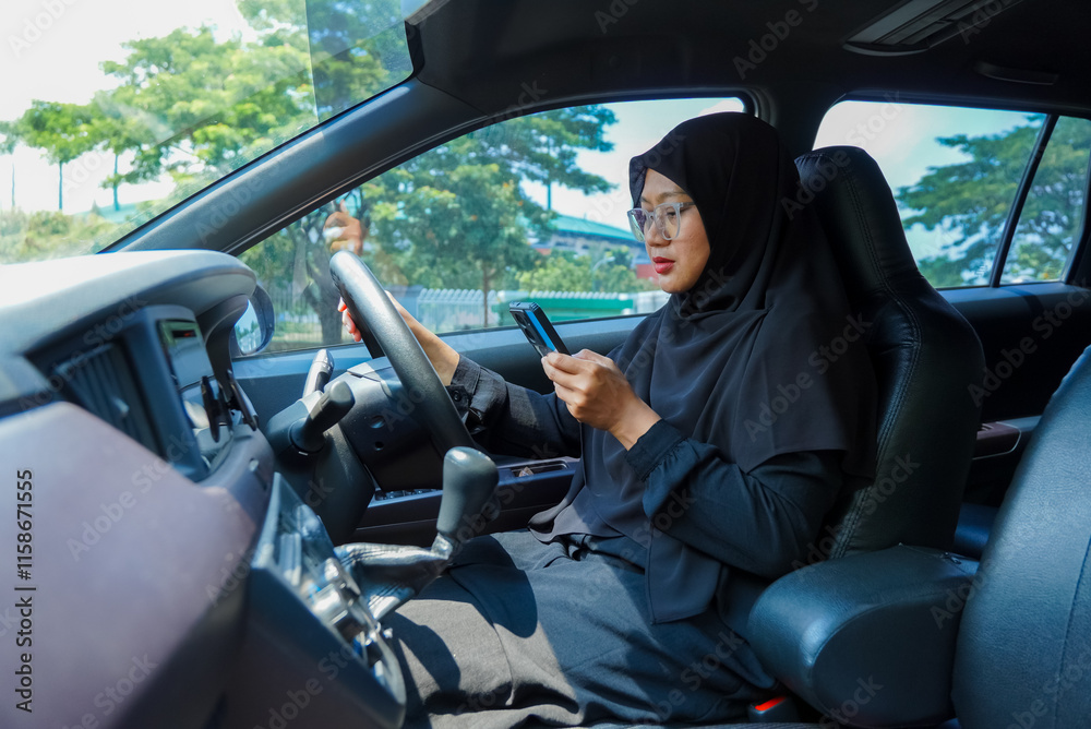 A woman is talking on her cell phone while driving a car. She is wearing a black hijab and is driving a white car A woman is talking on her cell phone while driving a car. She is wearing a black hijab and is driving a white car