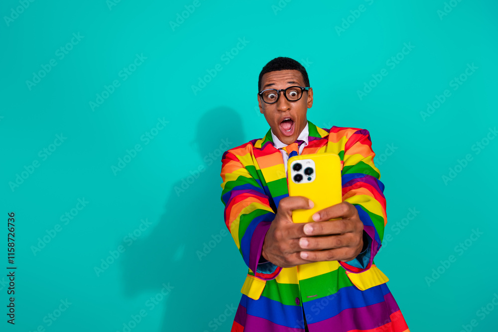 Stylish man in rainbow suit taking selfie with yellow phone on teal background Stylish man in rainbow suit taking selfie with yellow phone on teal background