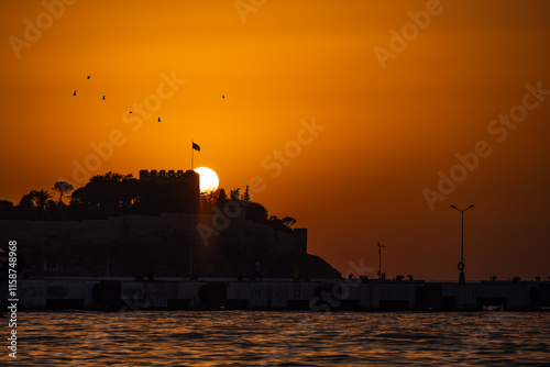 A stunning sunset behind a historic castle by the coast, with birds flying. Kusadasi, pigeon island sunset view. photo