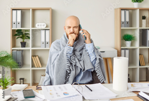Sick man sitting at desk coughing working, phone call, blowing running nose, suffer from flu or cold at home, ill male worker feels unhealthy struggle with influenza under blanket, employee healthcare