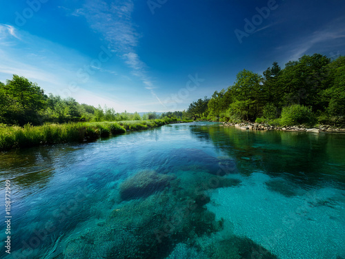 Crystal-clear river flows through lush greenery under a vibrant blue sky.  The calm water reveals a rocky riverbed. Tranquil scene of nature's beauty.