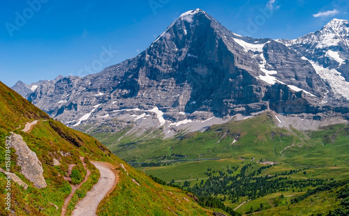 Tableau sur toile The Northern wall of Eiger peak in summer with clear blue skies and green meadows