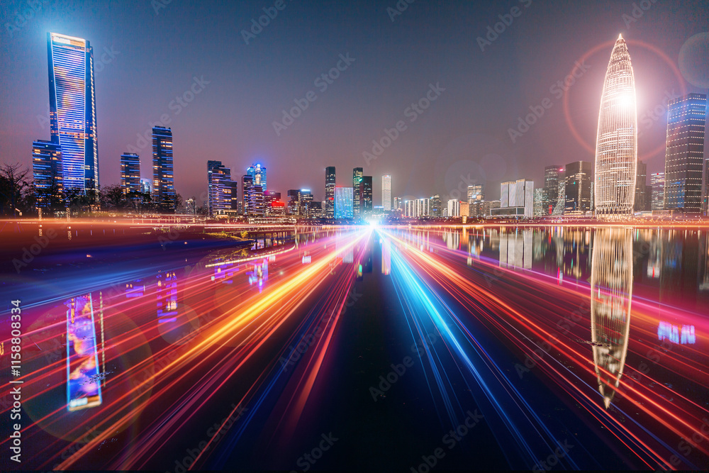 Naklejka premium Night scene of vibrant Shenzhen, China. A long exposure captures streaks of light from speeding vehicles on a highway, reflecting on calm waters, with a modern cityscape backdrop.