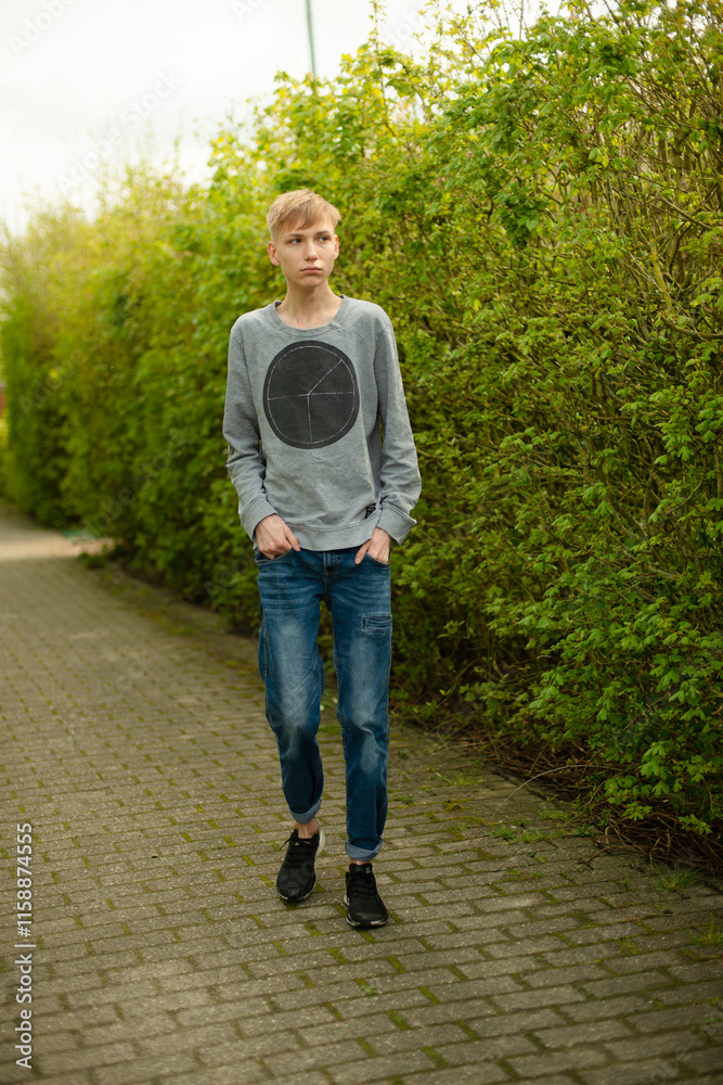 Fototapeta premium Smiling Blond Man in Blue Jeans and Gray Sweater Walking in Park Happy and Relaxed