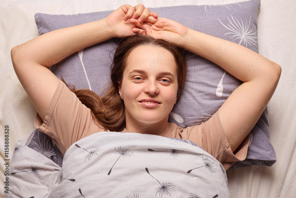 A woman lies in bed, her arms raised behind her head, smiling contentedly. The soft bedding and pillow create a cozy atmosphere in the room, capturing a moment of relaxation A woman lies in bed, her arms raised behind her head, smiling contentedly. The soft bedding and pillow create a cozy atmosphere in the room, capturing a moment of relaxation