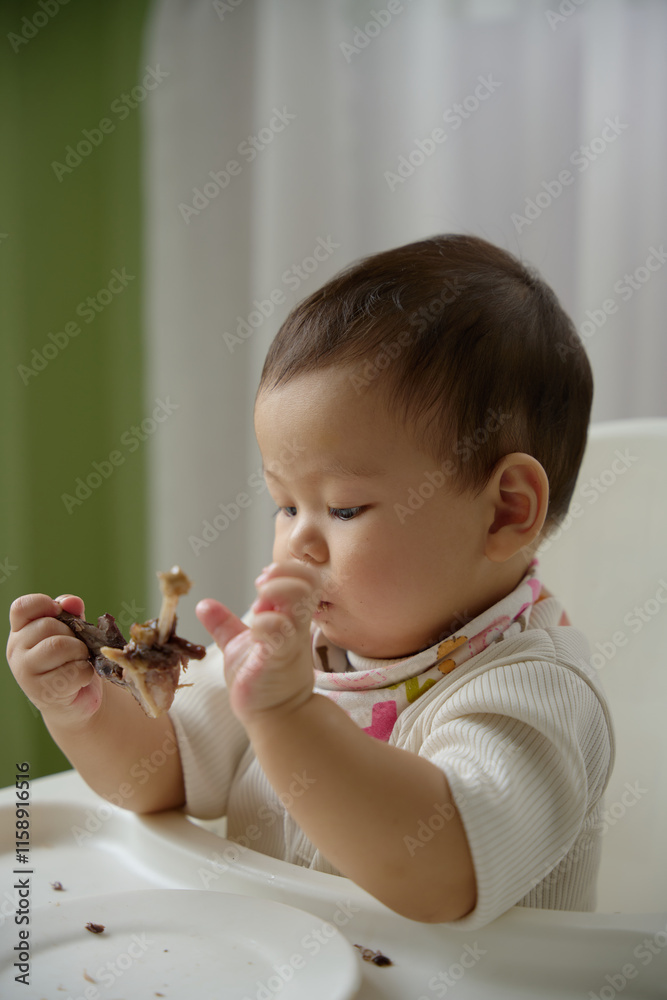 The baby is eating meat on the dining chair with a natural white background The baby is eating meat on the dining chair with a natural white background