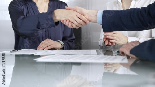 Business partners shaking hands after signing contract at glass table in office meeting, making a deal and closing agreement, close up of handshake