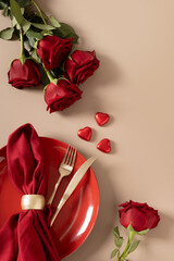 Valentine's day. Romantic dinner for date with red plate, chocolate sweets, romantic gift and red roses on beige background. Vertical menu card. View from above.