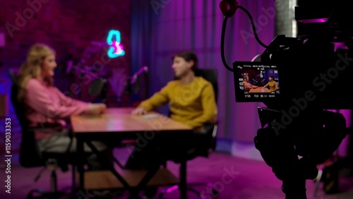 Backstage blurred shot of host and guest recording interview in loft podcast studio, creating digital content, camera on tripod filming at side, display pov.