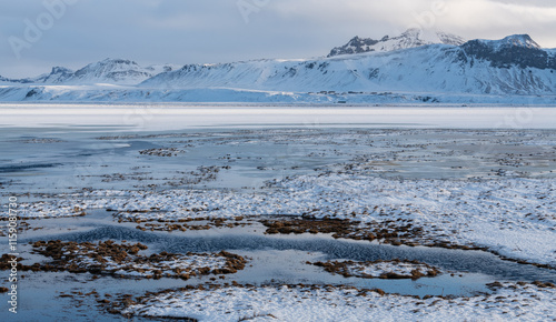 View on frozen sea and snowy volcanic mountains in the background, Iceland. Near Reynisfjara beach and reynisdrangar sea stacks, south coast of Iceland winter time. Ice and snow, remote location. Wond photo