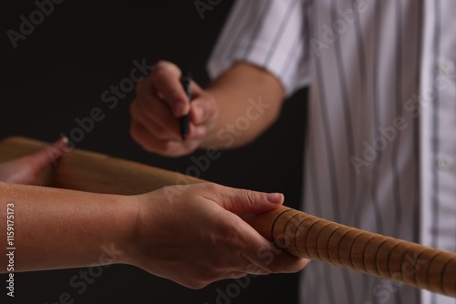 Baseball player signing autograph on bat against black background, closeup photo