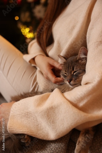 Woman with cute cat against blurred Christmas lights, closeup