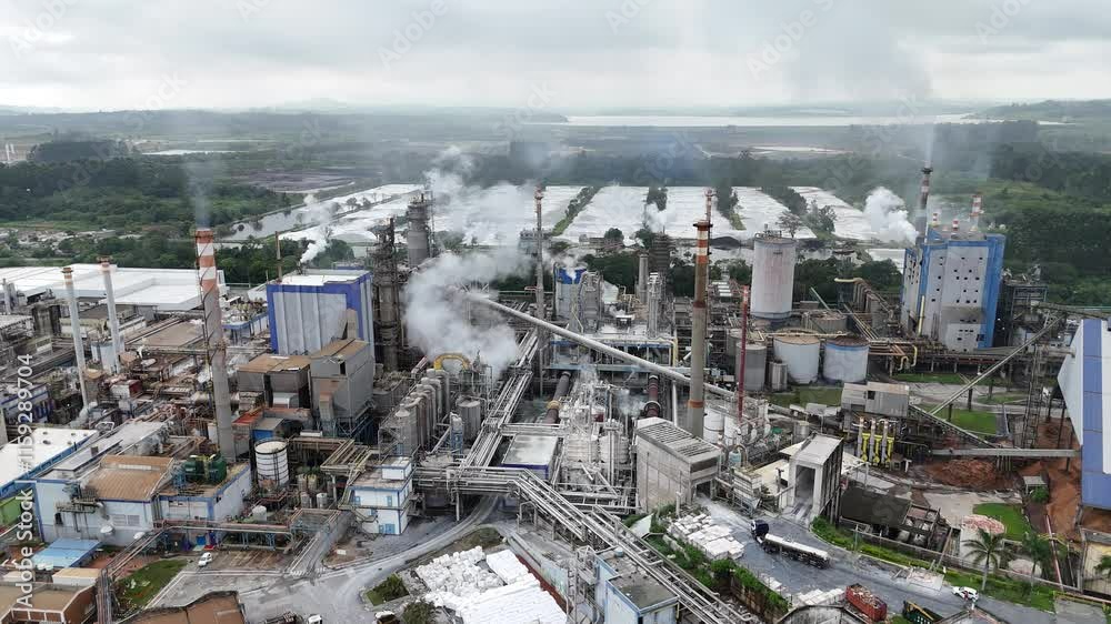 Visão aérea de uma indústria de papel e celulose, mostrando as fumaças e poluentes liberados durante o processo de produção. A cena reflete a dinâmica industrial e os impactos ambientais