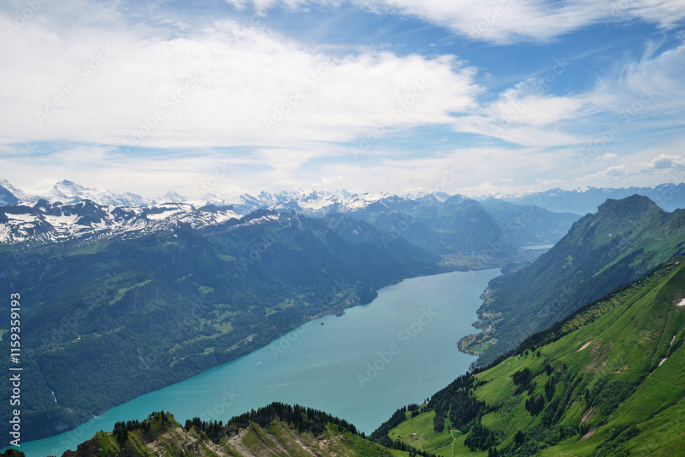 Fototapeta premium A breathtaking view of Lake Brienz in Switzerland, surrounded by majestic mountains and lush green hills, under a serene sky with wispy clouds.