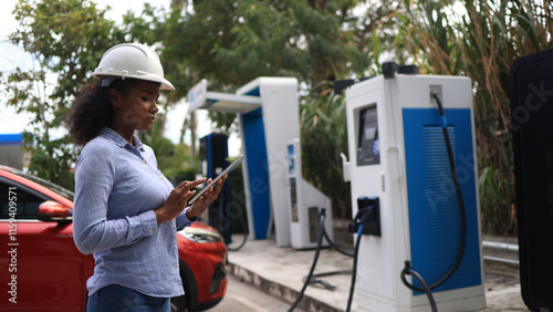 A Black female Electrical engineer is examining the electric vehicle charging pile, EV charger, green Zero carbon energy