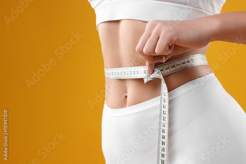 Weight loss. Woman measuring her slim waist with tape on yellow background, closeup. Space for text photo